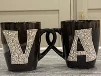 Personalized Crystal Initial Mug with letters "V" and "A" in sparkling crystals, ceramic, 450ml, handles intertwined, on a table.
