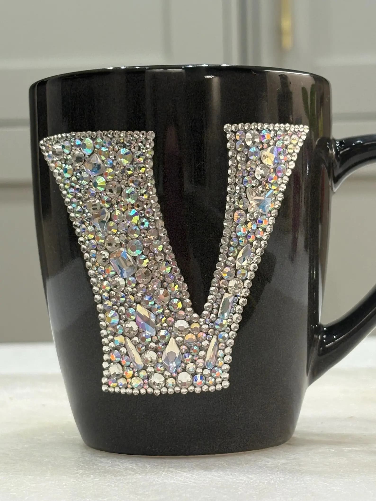 Personalized Crystal Initial Mug with a sparkling "V" on a black ceramic cup, showcasing intricate hand-decorated crystals.