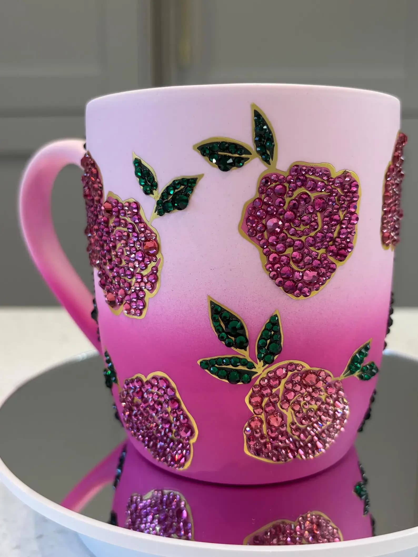 Sparkling Crystal Flower Mug with pink gradient and rhinestone floral design, shown close-up on a mirrored surface.